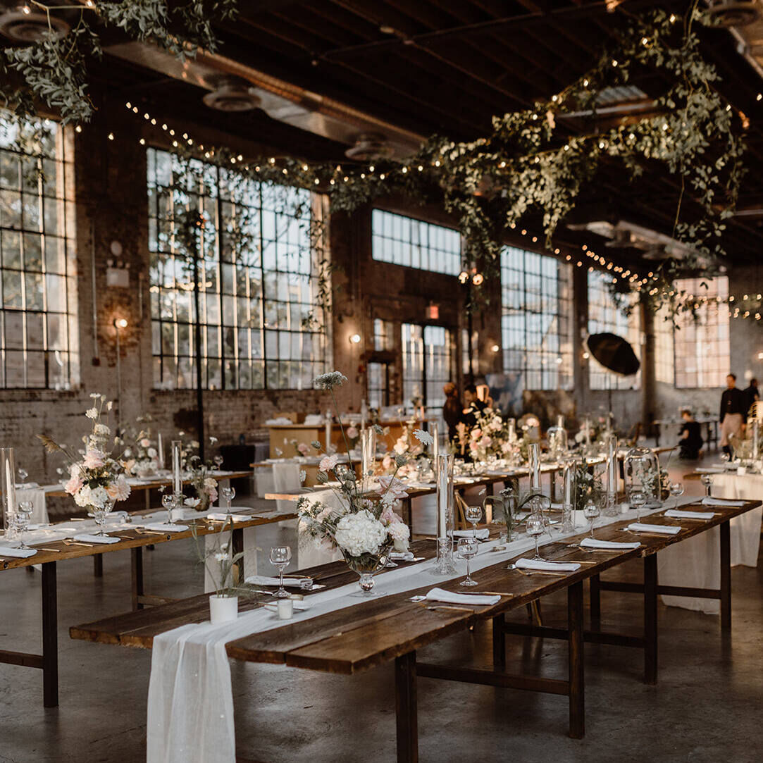 An industrial wedding venue (99 Scott) set up for a reception, with big windows, twinkle lights, long tables, and brick walls.