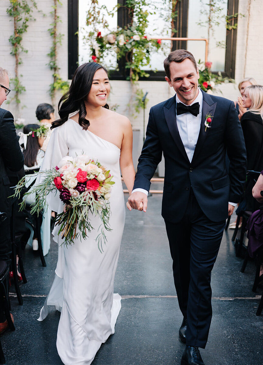 Industrial Wedding Venues: A bride and groom smiling, holding hands, and walking back down the aisle together at 501 Union.