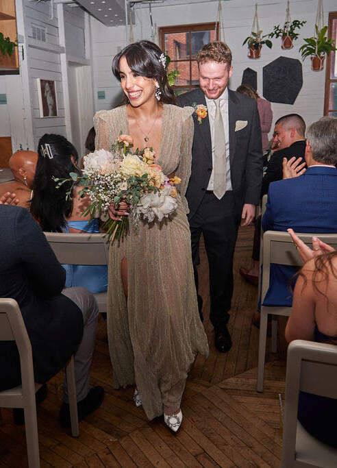 Industrial Wedding Venues: A bride and groom smiling, holding hands, and walking back down a narrow aisle together at Sunday in Brooklyn.