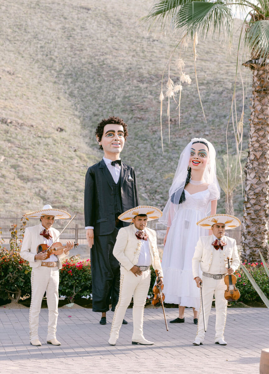 Latinx Heritage: Two oversized puppets, called mojigangas standing behind three members of a mariachi band.