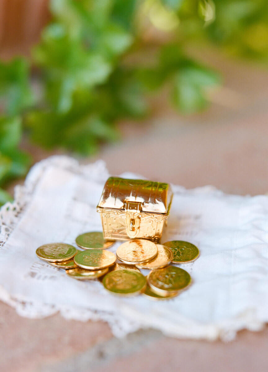 Latinx Heritage: Gold coins and a tiny gold trunk-like container on top of a lace-trimmed cloth.