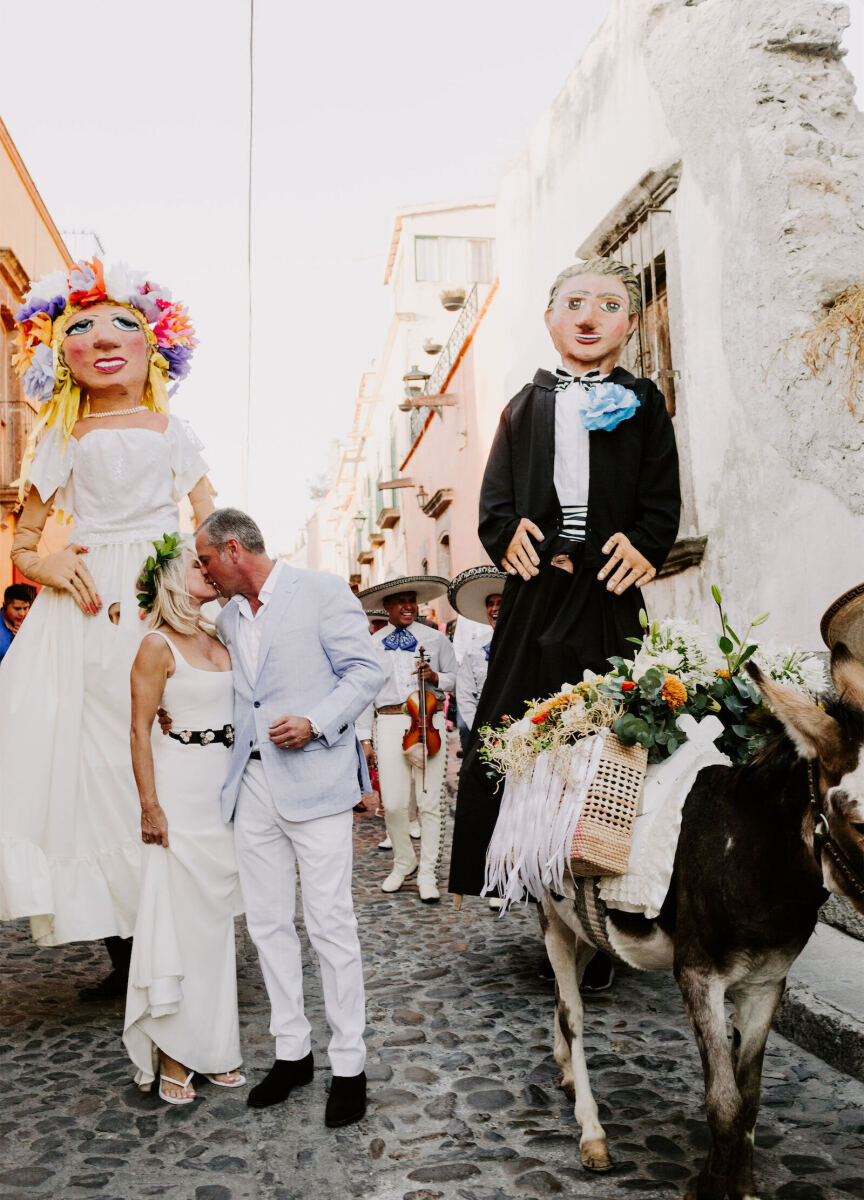 Latinx Heritage: A bride and groom kissing with mojigangas and a mariachi band behind them.