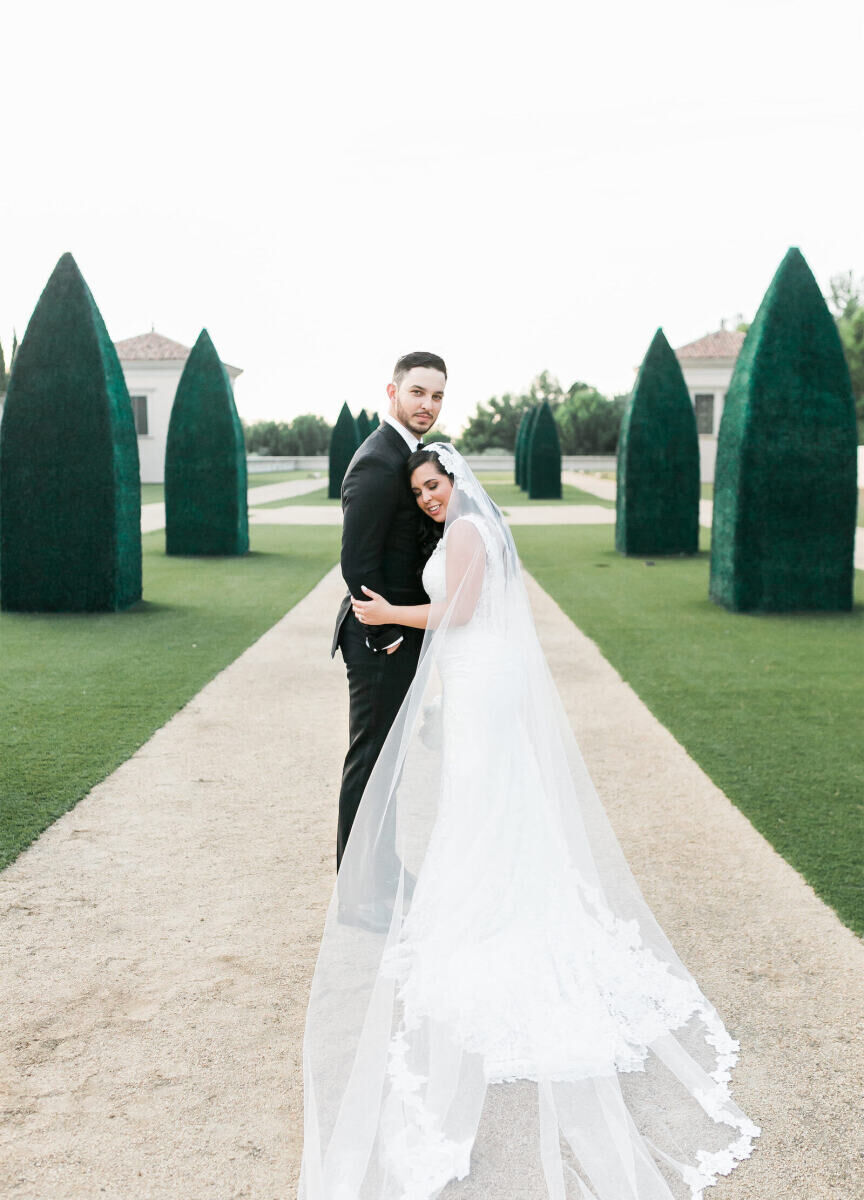 Latinx Heritage: A bride and groom embracing near hedging and a pathway in California.