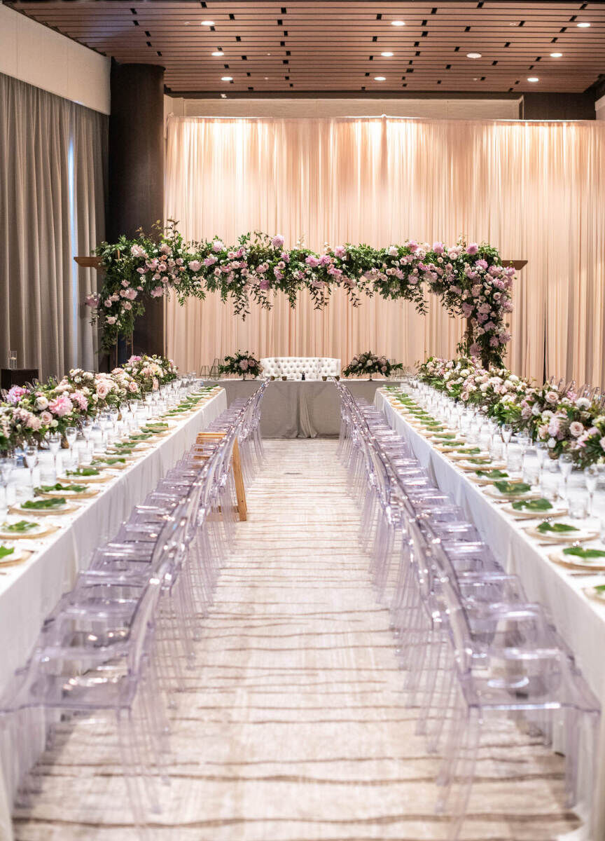 Marriott Wedding: An indoor reception space with two long rectangular tables leading up to a sweetheart table with a large floral installation overhead. 