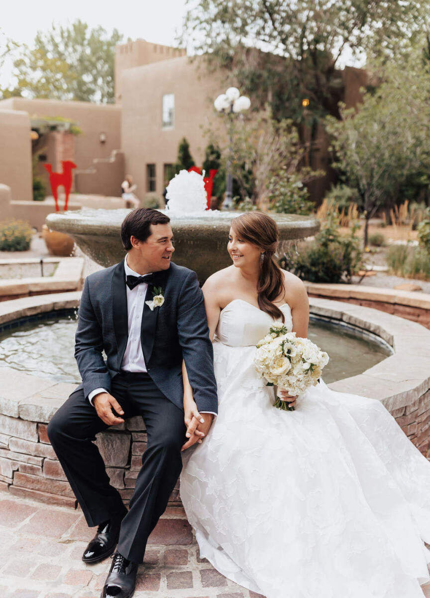 Marriott Weddings: A wedding couple sitting on the side of a fountain and smiling at each other in Santa Fe, New Mexico