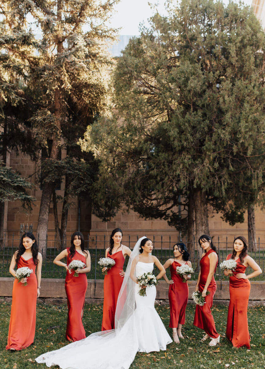 Marriott Weddings: A bride posing with her bridesmaids who are wearing red in an outdoor setting with trees in the background.