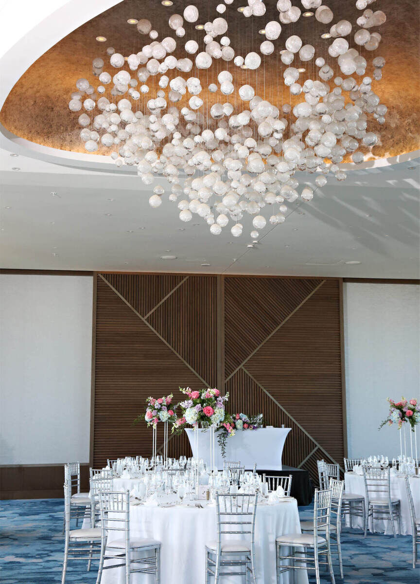 Marriott Weddings: An indoor reception setup with an elaborate white hanging installation coming from a gold ceiling, round tables, and blue carpeting.