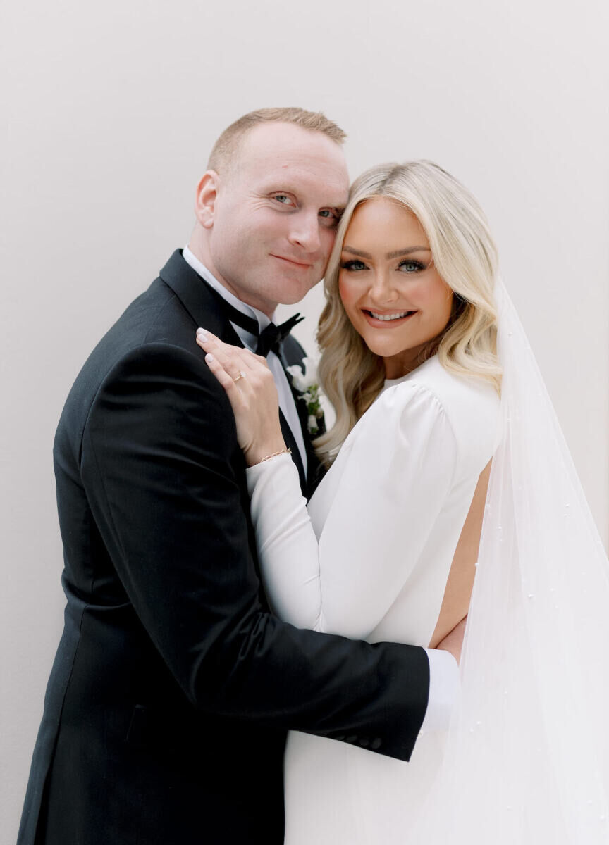 A groom and bride embrace and smile in a portrait on the day of their modern California wedding.