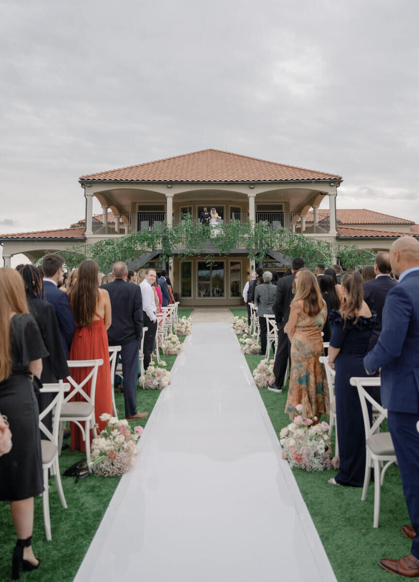 A bride and her father overlook the guests seated at the ceremony of this modern fairytale wedding before walking down the aisle.