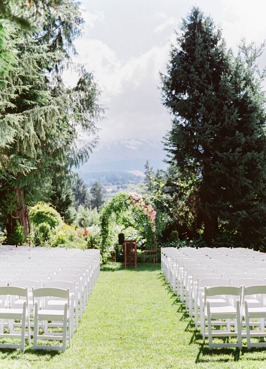 Mountain Wedding: A wedding ceremony setup with white chairs, a greenery-covered arch and a view of the mountains.