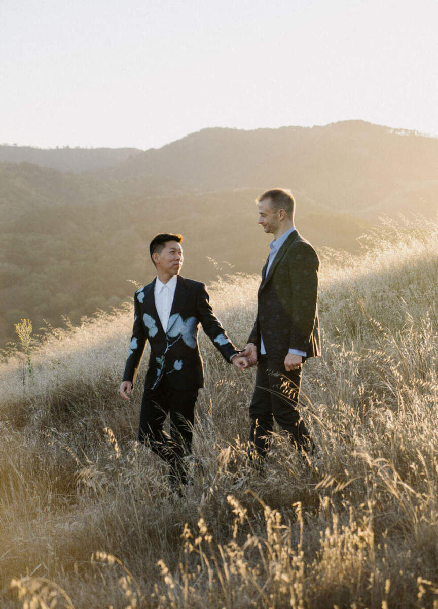 Mountain Wedding: Two grooms holding hands and smiling at each other on a hill in California.