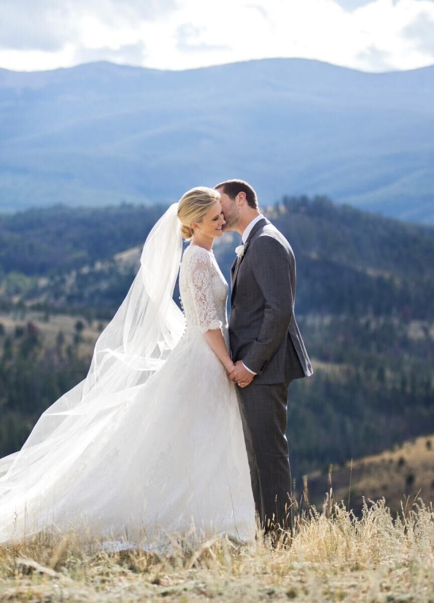 Mountain Wedding: A bride smiling as a groom kisses her on the cheek in a mountainous area in Montana.