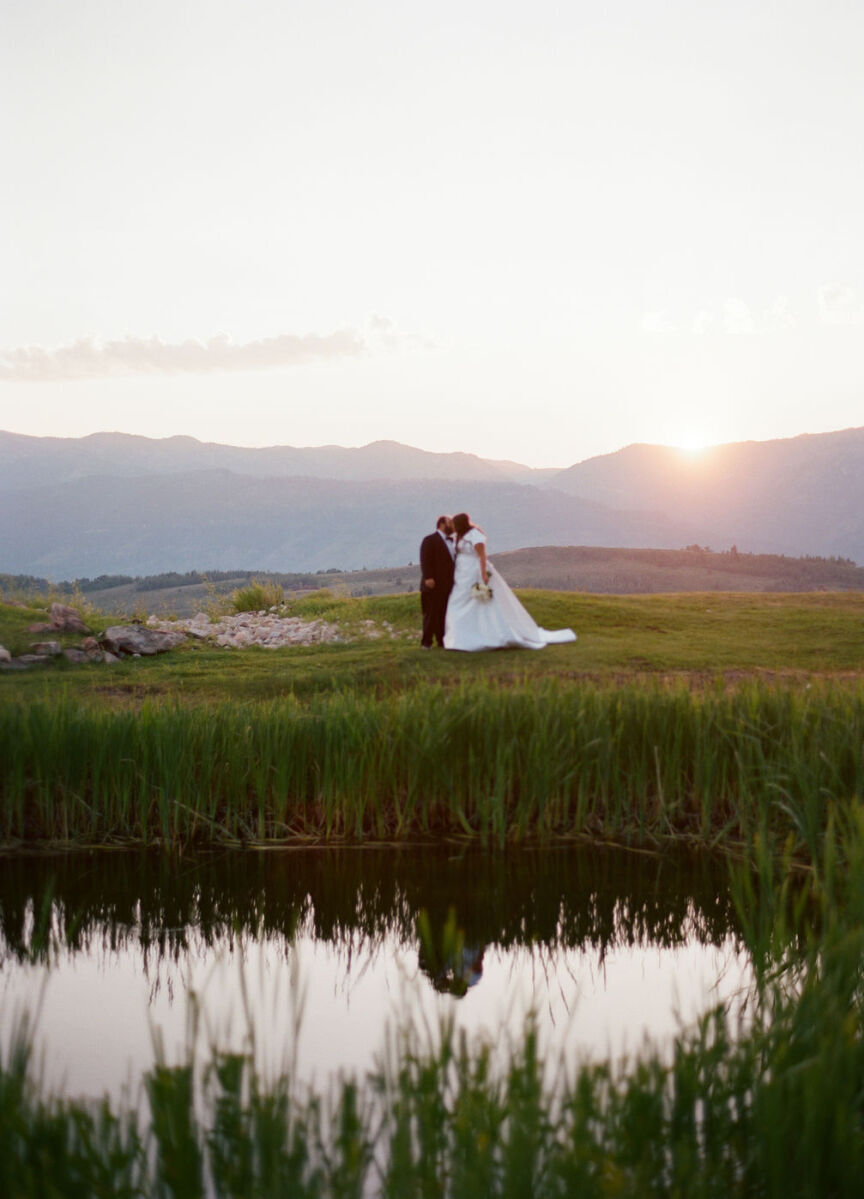 Mountain Wedding: A wedding couple kissing in a distant area, beyond a small body of water, and with mountains in the background.