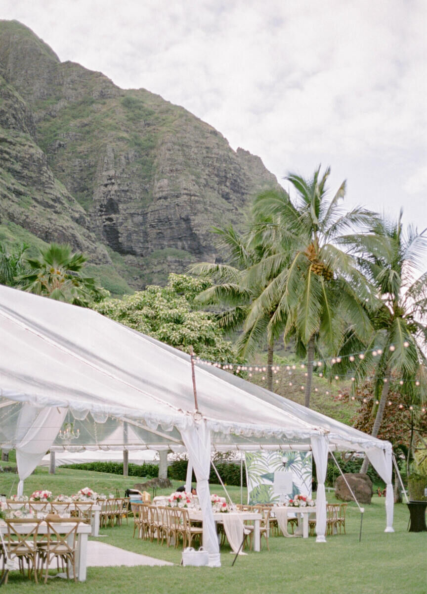 Mountain Wedding: An outdoor tented reception area in Hawaii, with palm trees and a mountainous cliff in the background.