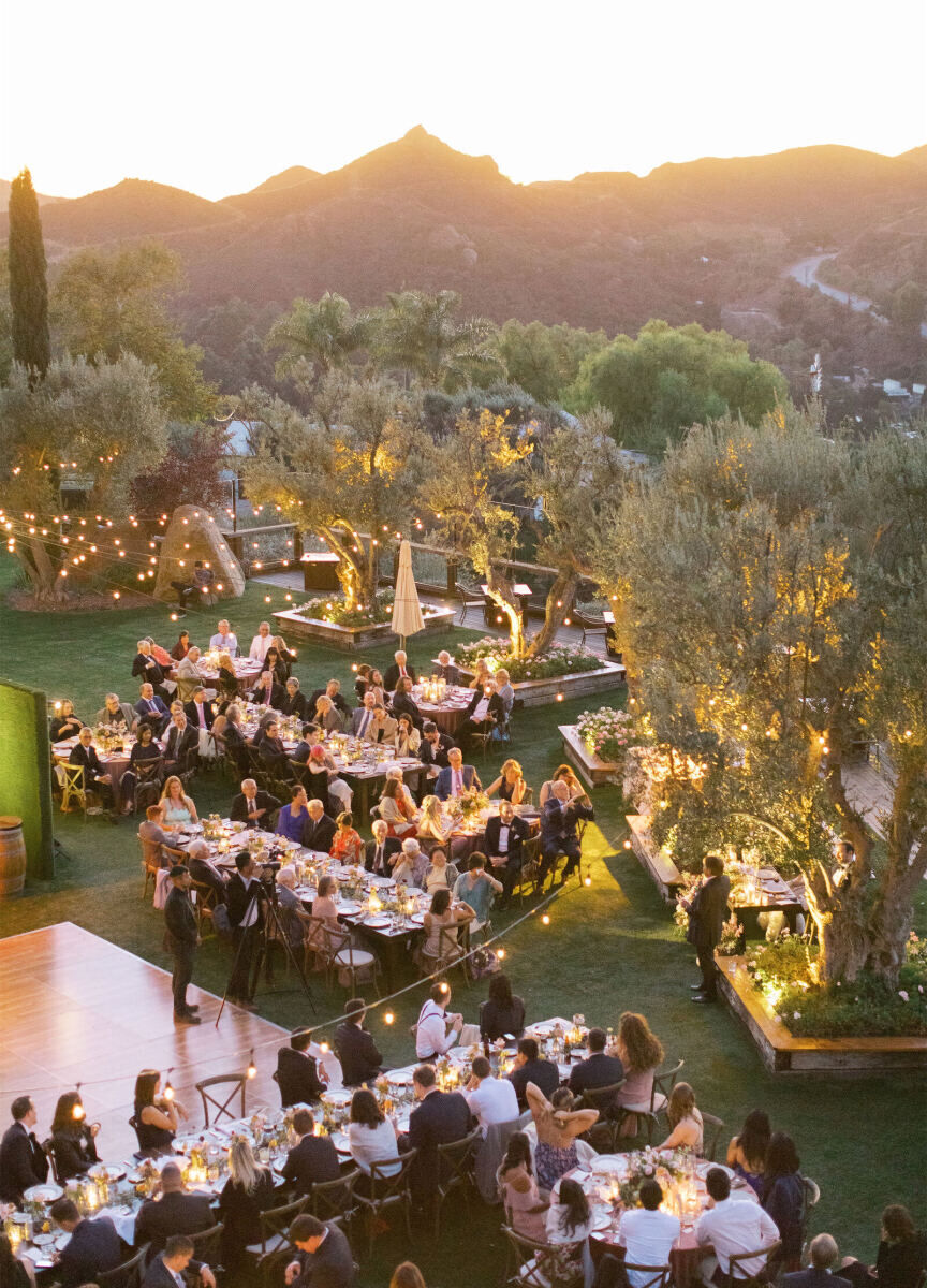 Mountain Wedding: An outdoor reception setup at dusk, with a dance floor, multi-sized tables, string lights, and trees and mountains in the background.