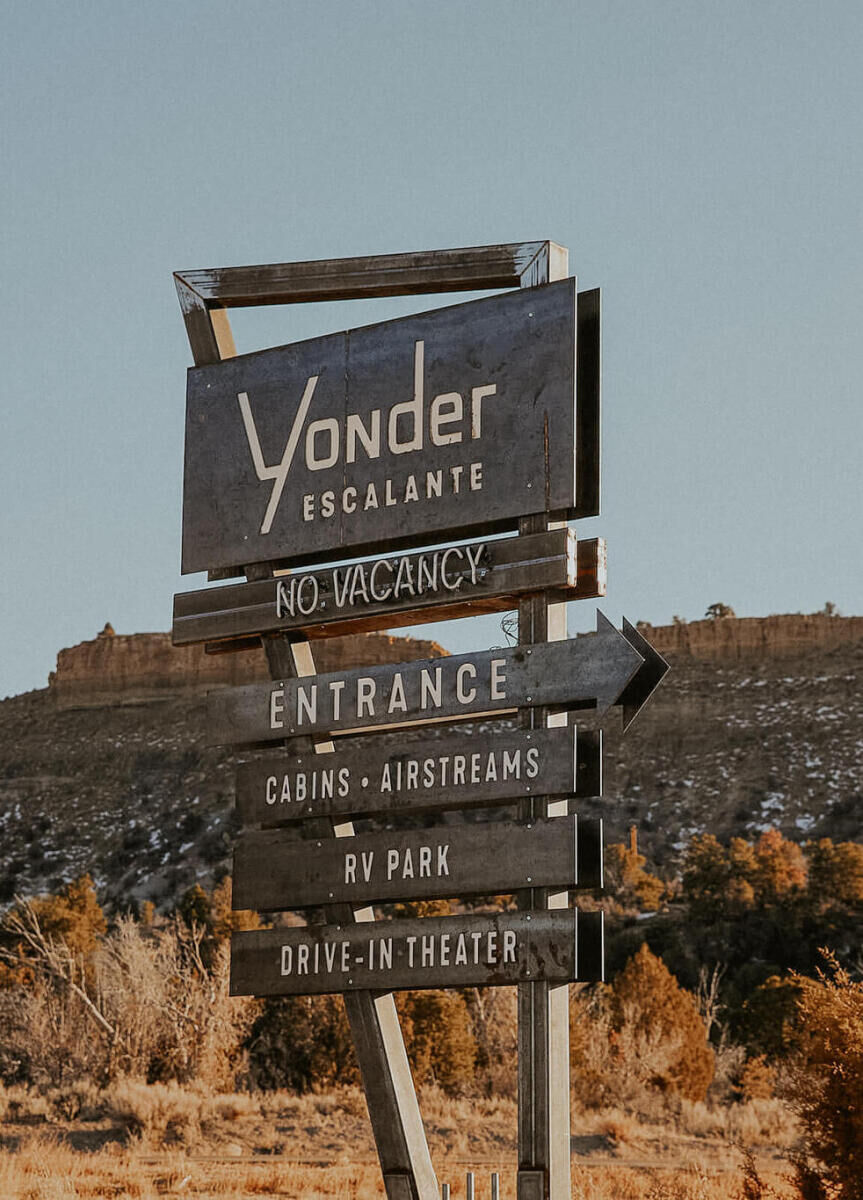 Mountain Wedding: A sign for Yonder Escalante, which includes a light-up vacancy sign, and directions to the entrance, cabins and airstreams, RV park, and drive-in-theater.