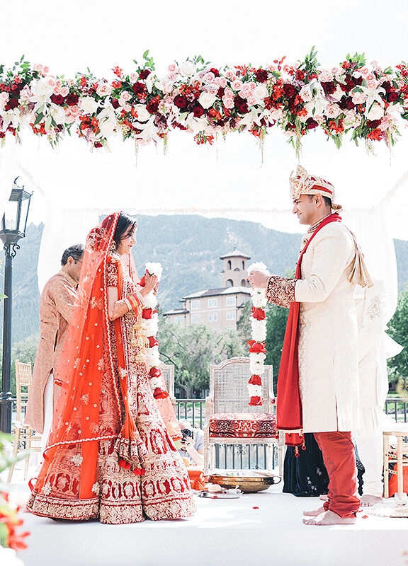 Mountain Wedding: A wedding couple holding garlands of flowers under a pergola at an outdoor wedding ceremony.