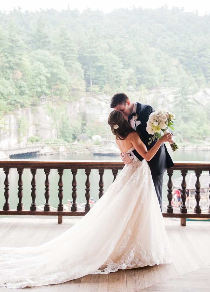 Mountain Wedding: A wedding couple kissing on a balcony overlooking the mountains covered in forestry.