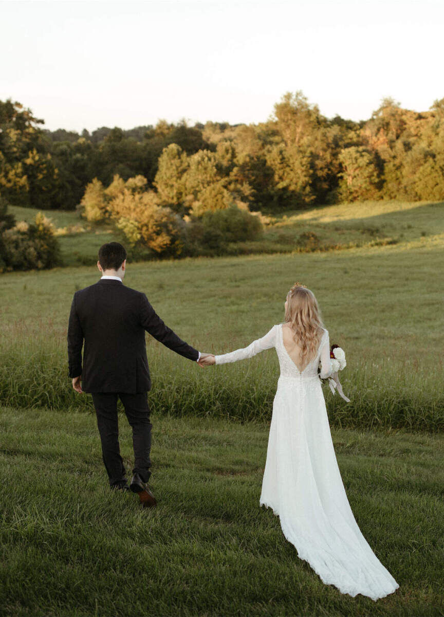 Mountain Wedding: A wedding couple holding hands with their backs facing the camera, and walking toward the trees and mountains in the background.