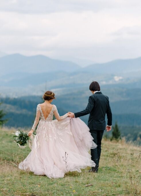 Mountain Wedding: A wedding couple walking away from the camera, holding hands, and toward a mountain range in Colorado.