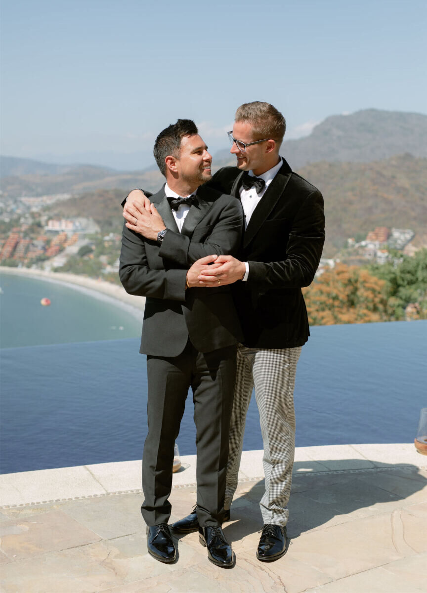 Mountain Wedding: Two grooms wearing suits with bowties, and a pool and mountains in Mexico behind them.