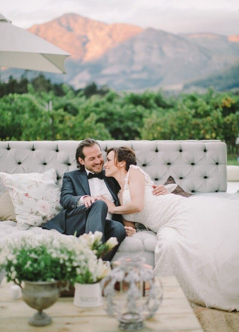 Mountain Wedding:  A wedding couple snuggling and smiling on an outdoor couch with a view of the mountains in South Africa behind them.