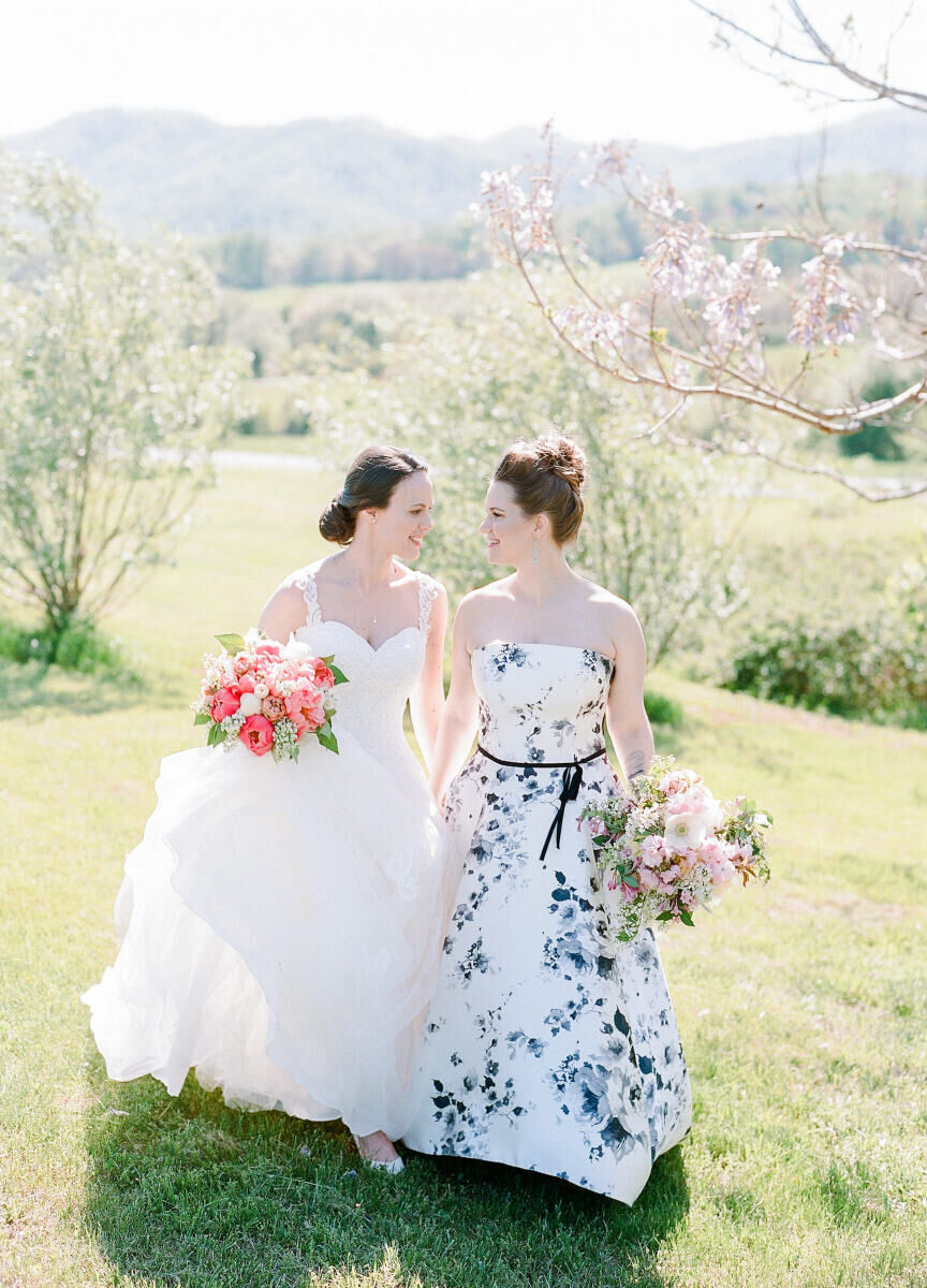 Mountain Wedding: Two brides with bouquets smiling and facing each other, with hills and mountains behind them.