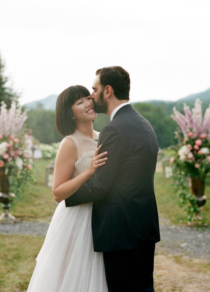 Mountain Wedding: A groom kissing a bride, with floral arrangements and mountains in the background.