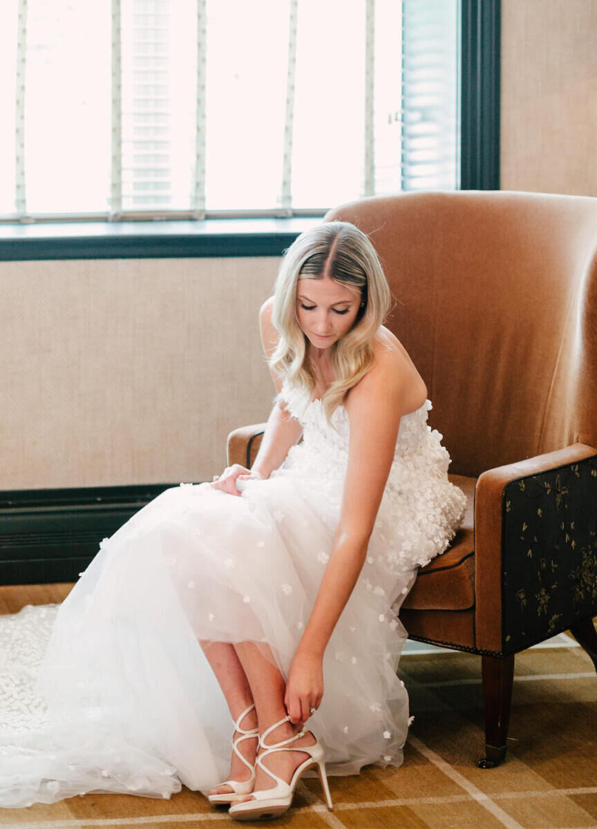 Mountain wedding details: 
Bride sitting in a chair, wearing her wedding dress, buckling her shoe.