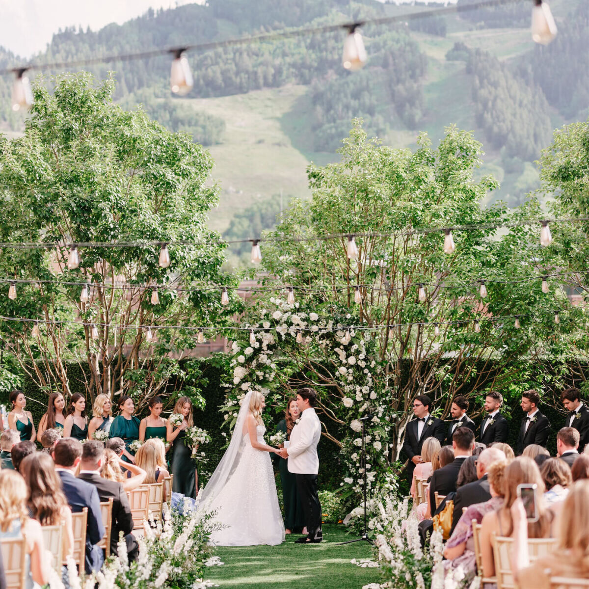 Mountain wedding details: Wedding couple holding hands at their green-and-white wedding ceremony in the courtyard of Hotel Jerome.