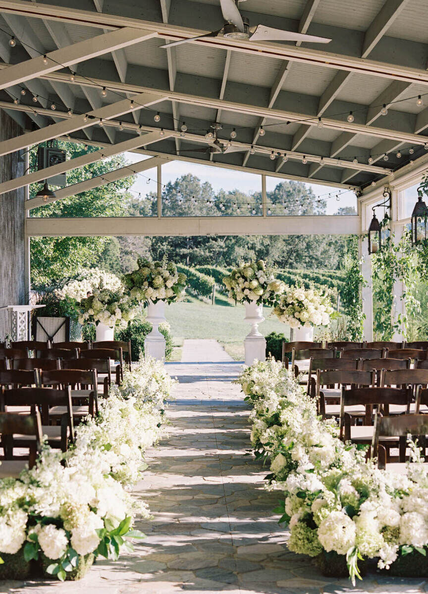 Pippin Hill Farm: An indoor ceremony setup on a terrace with wooden chairs and white arrangements lining the aisle.