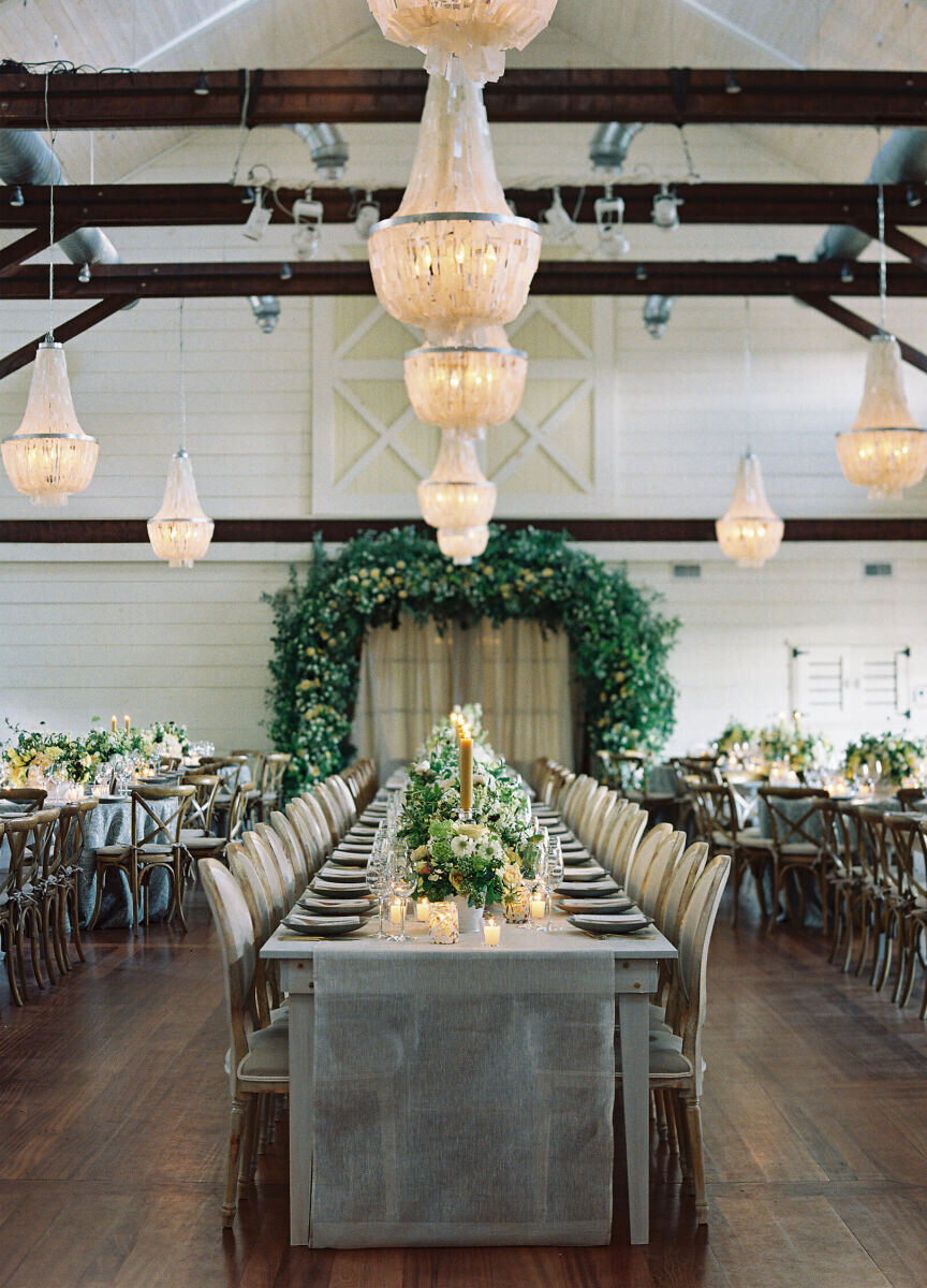 Pippin Hill Farm: Several white chandeliers hanging from the ceiling at an indoor reception area with an arch of greenery and florals in the back of the room.