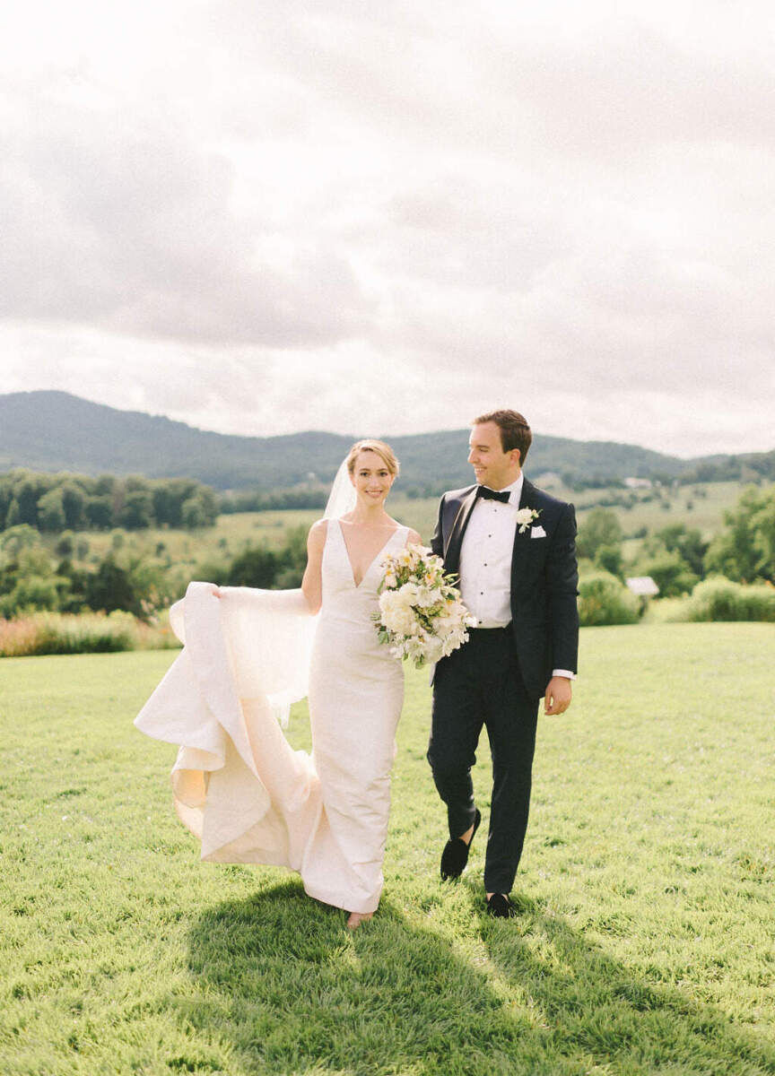 Pippin Hill Farm: A groom looking at a bride holding up her train on a hill at a wedding in Virginia.