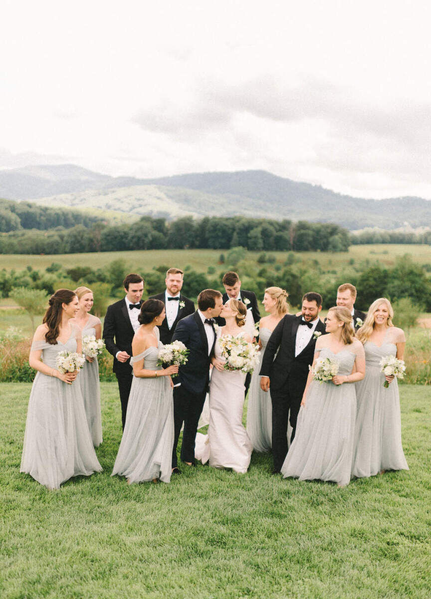 Pippin Hill Farm: A bridal party dressed in tuxedos and pastel bridesmaid dresses watching as a bride and groom kiss.