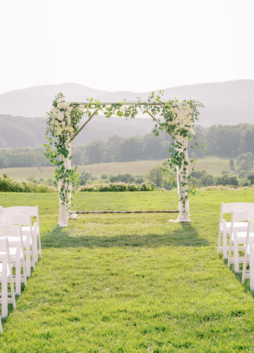 Pippin Hill Farm: A chuppah with greenery at the end of an aisle with white chairs on either side, overlooking the Blue Ridge Mountains in Virginia.