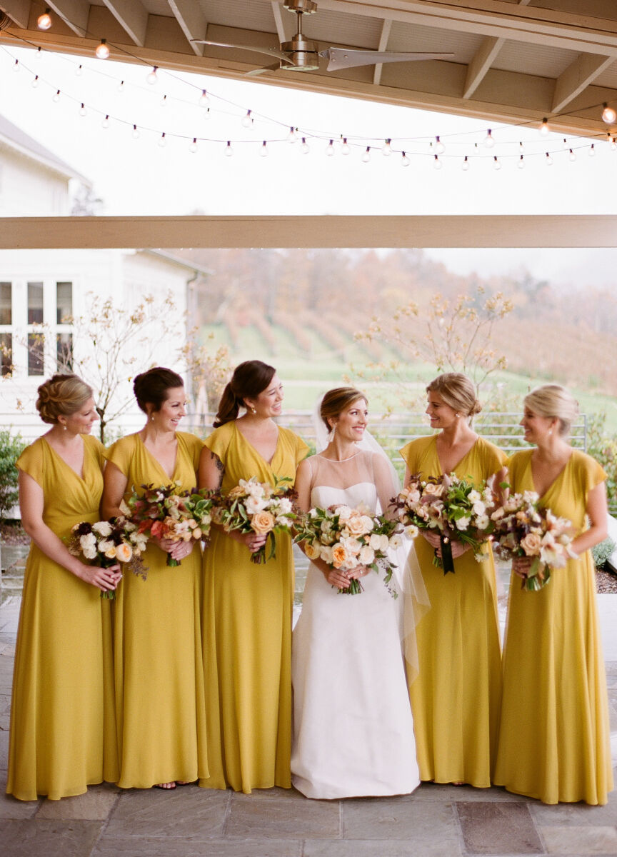 Pippin Hill Farm: A bridal party dressed in mustard yellow bridesmaids dresses posing with the bride under an awning adorned with string lights.