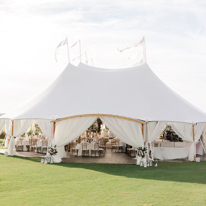 Tented wedding reception, featuring bright white sailcloth tent with tied back draped entrances on a well-manicured golf course