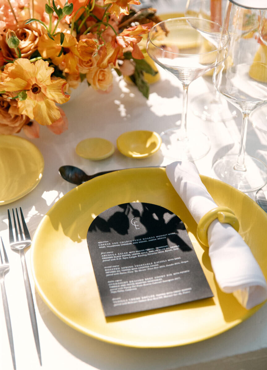 An all-yellow placesetting at a rainbow wedding is complete with a rolled-up napkin accessorized with a fun napkin ring and a black, rounded-edge menu.