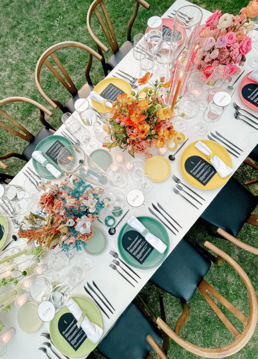 A rainbow wedding reception set with four different color combinations for place settings and corresponding floral centerpieces.