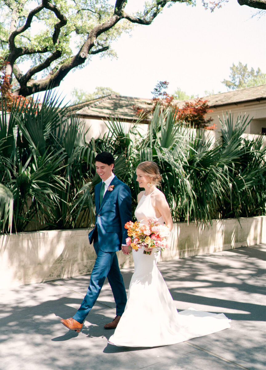 A bride and groom walking hand in hand on the tree-lined sidewalk at their backyard wedding.