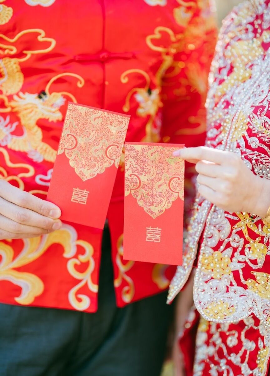 Bride in red wedding dress and wedding couple holding up red wedding invitations 