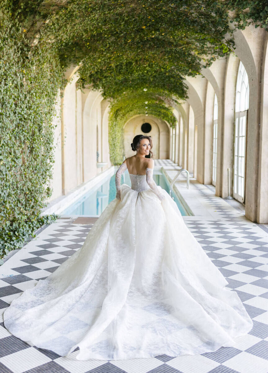 Royal Wedding Dresses: A bride walking down a grand corridor with her back to the camera. Her white wedding gown has a long, flowing train.