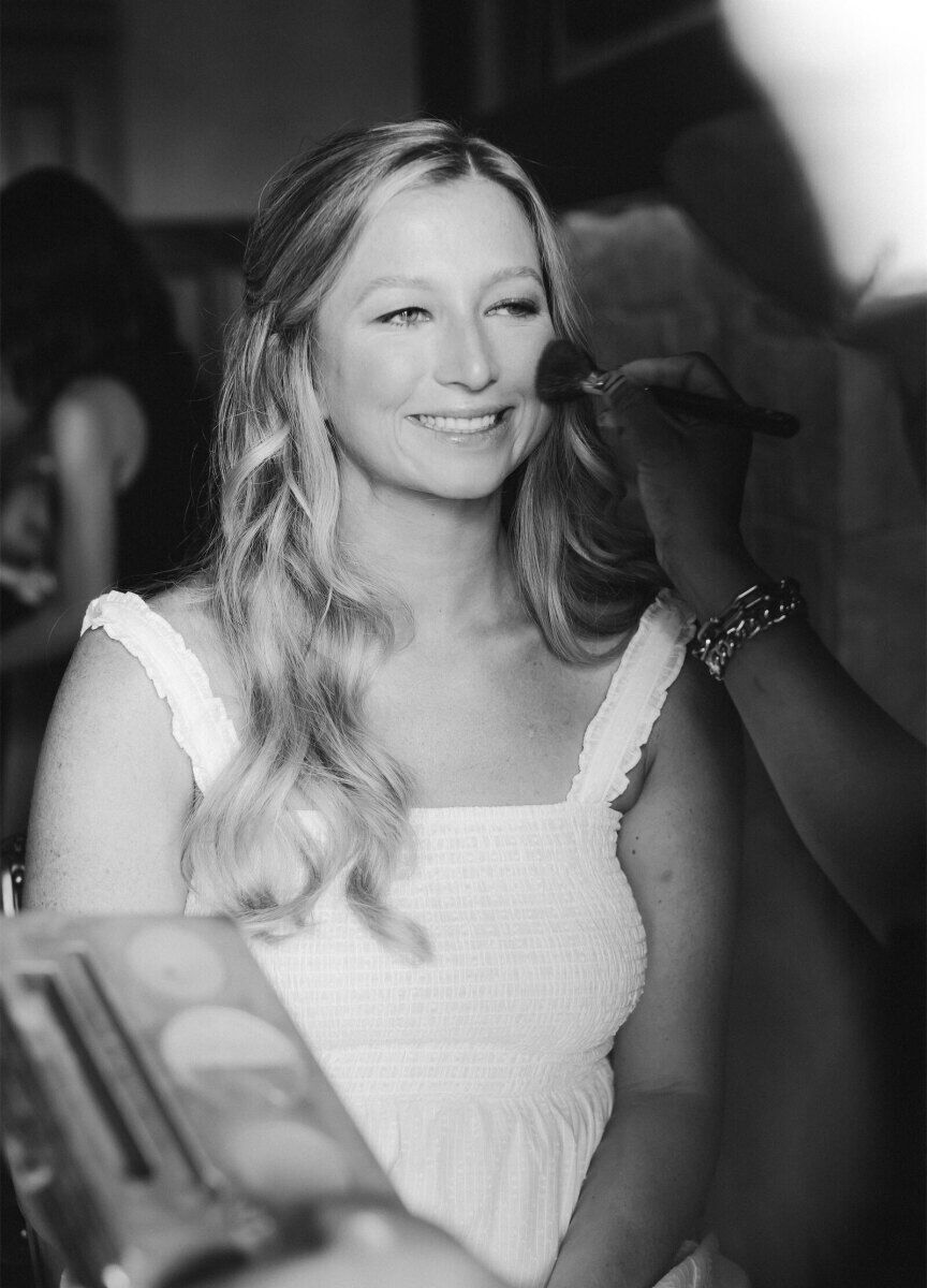 A bride gets her hair and makeup done on the morning of her rustic outdoor wedding.