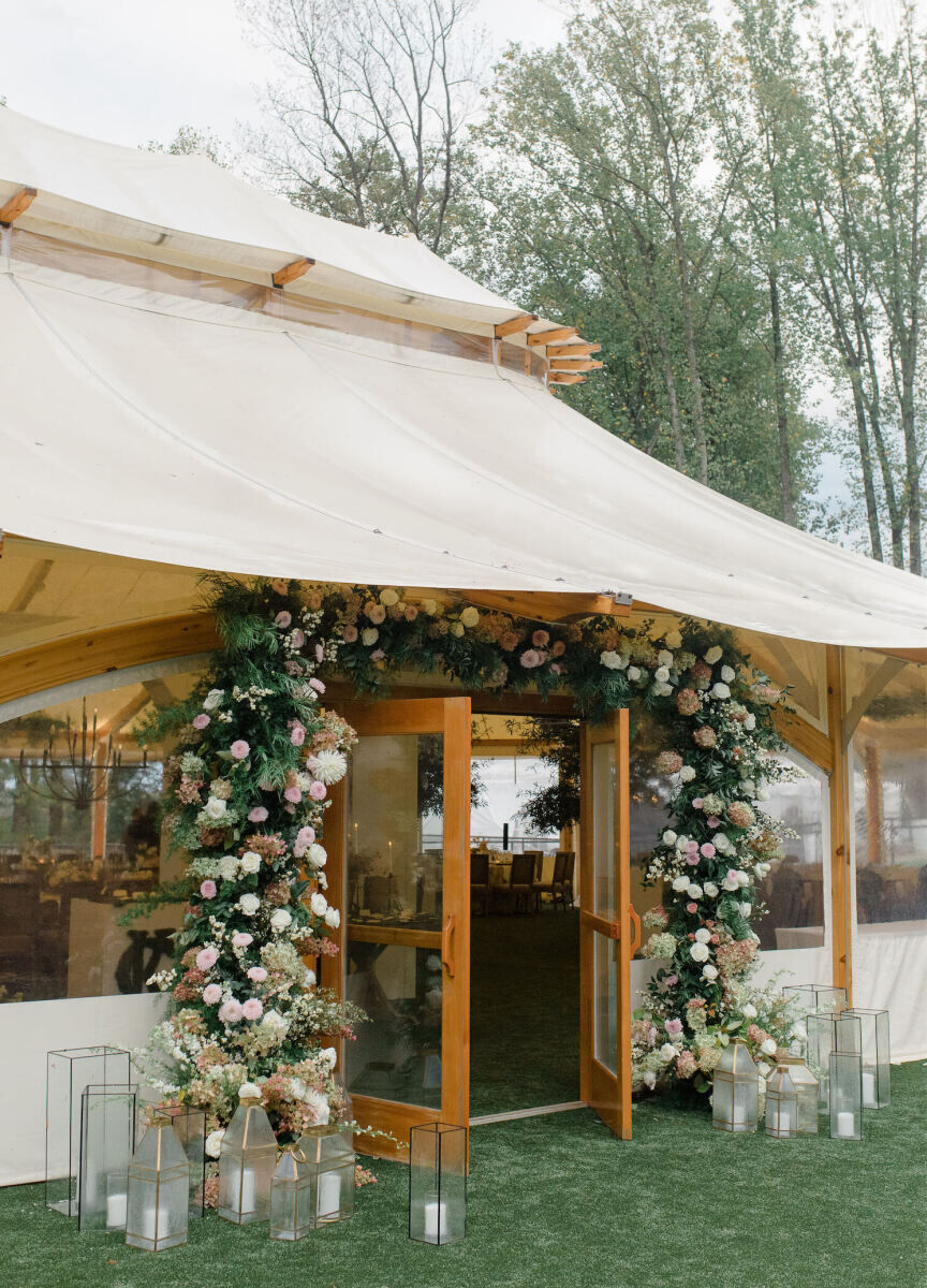 A floral arch decorates the entryway of a tent for the reception of a rustic outdoor wedding.