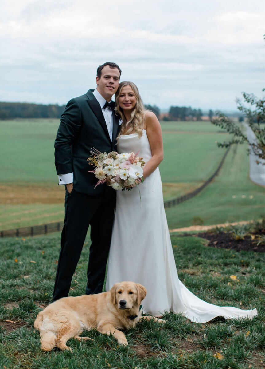 A couple and their dog pose for a portrait on the day of their rustic outdoor wedding, which took place at a lodge in Virginia.