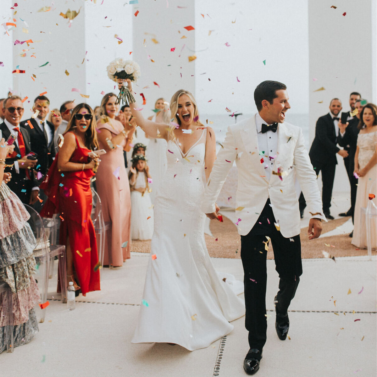 SEO for Wedding Venues: A wedding couple celebrating at a modern outdoor ceremony space in Mexico, with rainbow-colored confetti raining down on them.