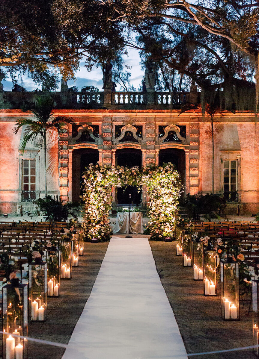 SEO for Wedding Venues: An outdoor ceremony setup at dusk in Miami, with wooden chairs, a floral arch, and candles lining the white aisle.