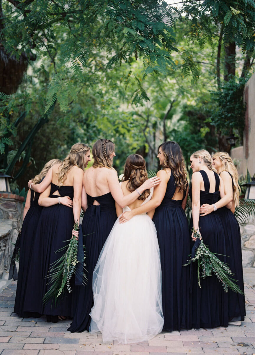 SEO for Wedding Venues: A bride and her bridesmaids, who are all in black, standing on a stone patio with trees all around them.