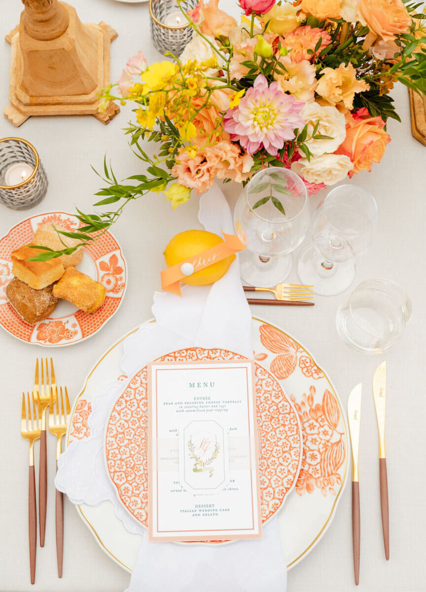 An orange, white, and yellow table at a Tuscan wedding reception, with guests' names pinned to fresh lemons.