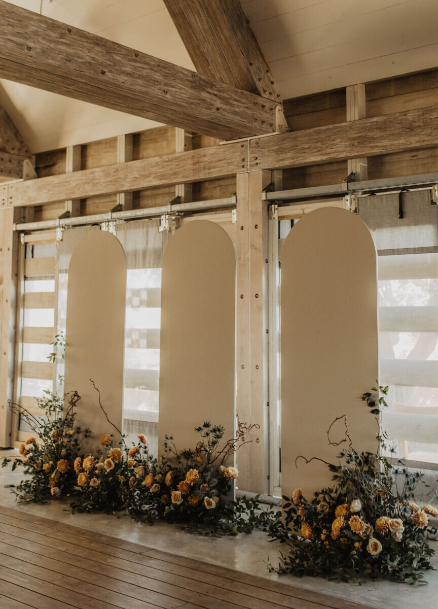 Three curved panels anchored by wild arrangements of flowers, greenery, and vines, created the ceremony space inside the venue where this untraditional wedding ceremony took place.